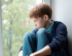 kid-at window young teenage boy sitting at the window looking sad