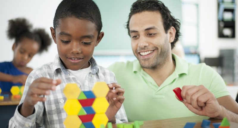 A teacher is helping a student with stacking blocks in class.