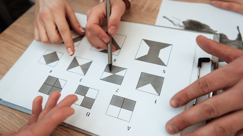 Man hand holds pencil to make a mark on test. Man's hand holds pencil to make a mark on graphic test. Man is passing psychological graphic test. Passing of psychological test with figures on sheet of paper.